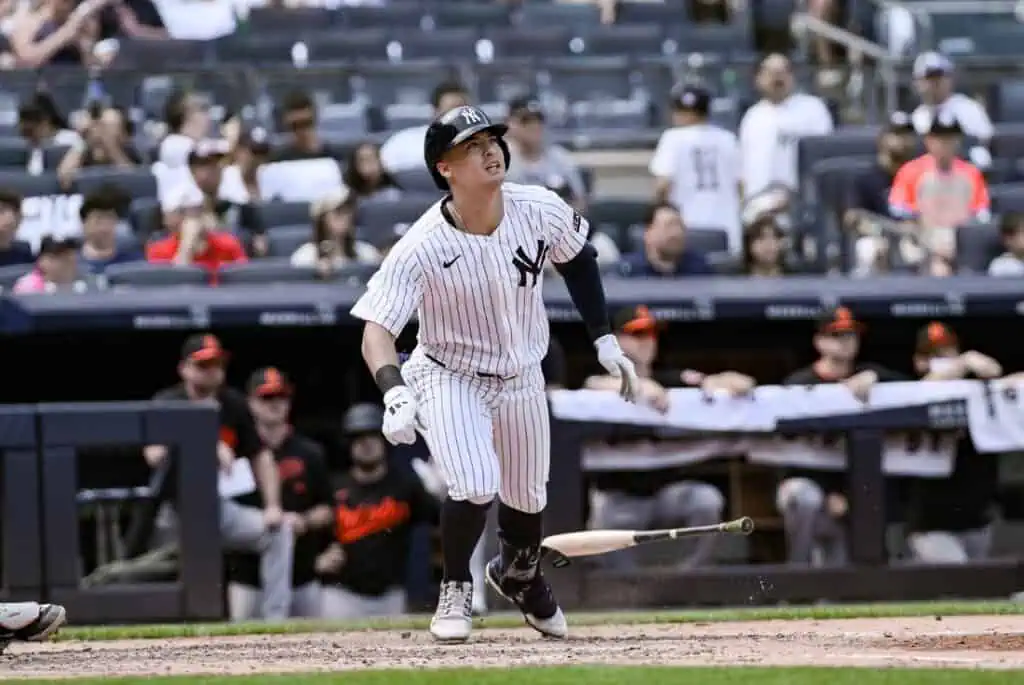 A baseball player in a striped Yankees uniform swings a bat, with the crowd and team members