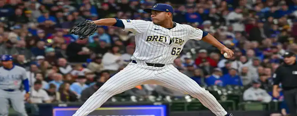 Milwaukee Brewers pitcher in full stride delivering a pitch during a game, wearing a white pinstripe uniform on a crowded field.
