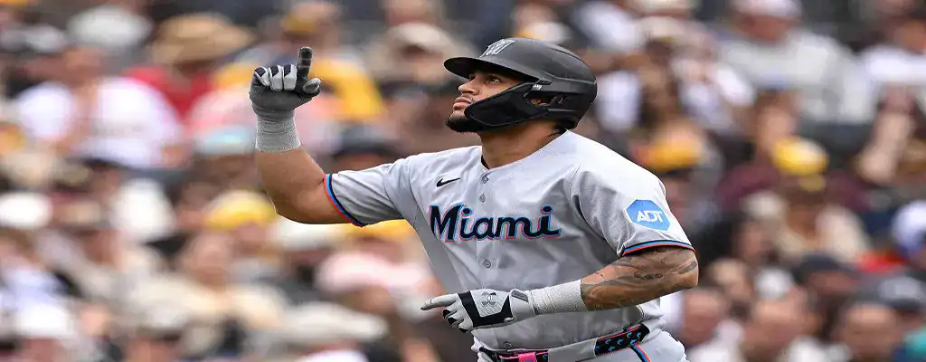 Miami Marlins player points upward while celebrating a run during a game, wearing a gray jersey and black helmet with crowd in the background.