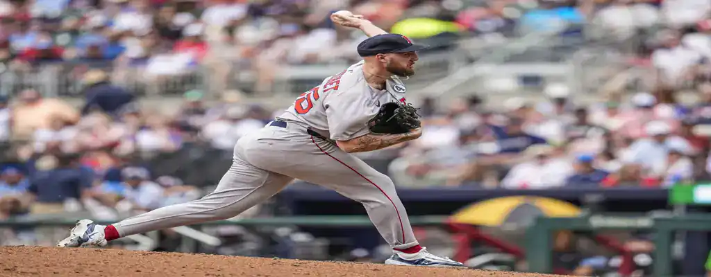 red sox pitcher in full extension delivering a pitch during a game, wearing a gray uniform with red accents.