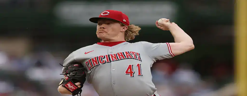 Cincinnati Reds pitcher captured mid-throw in a close-up shot, wearing a gray uniform and red cap during a game.