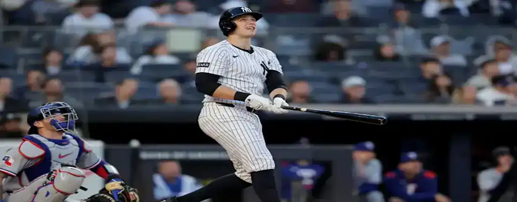 New York Yankees batter watches his home run fly, standing in the batter's box in pinstriped uniform during a game.