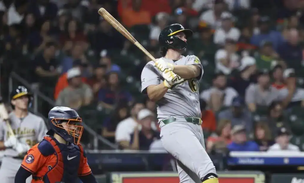 A baseball player in a grey uniform swings a bat, as a catcher in orange gear prepares for the play, amid a cheering crowd.