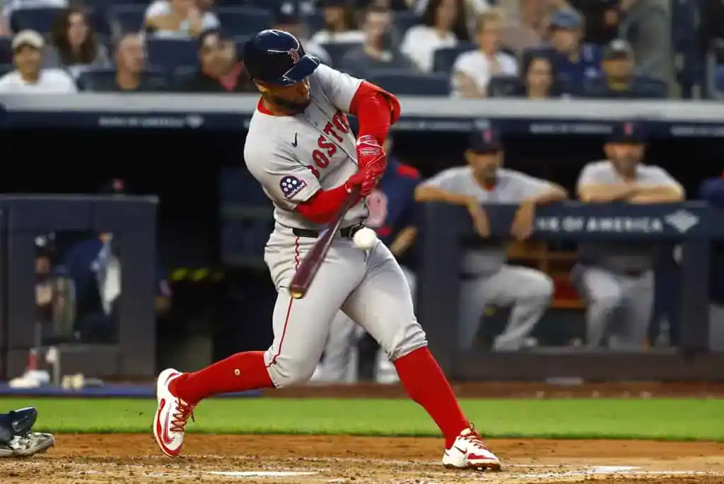 A Boston Red Sox player in a grey road uniform swings a bat and makes contact with the ball.