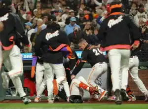 A group of players in Giants uniforms surrounds a teammate on the ground during a tense moment in a baseball game.