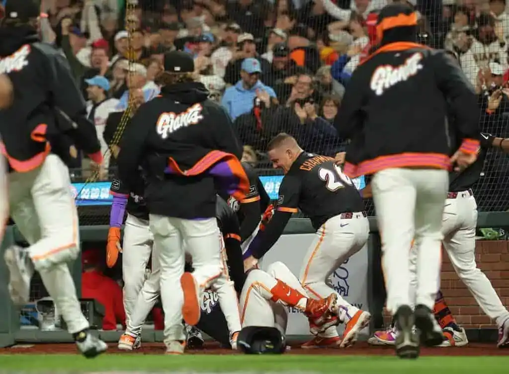 A group of players in Giants uniforms surrounds a teammate on the ground during a tense moment in a baseball game.