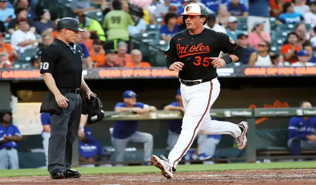 Baltimore Orioles player scores a run as the umpire looks on during a game against the Toronto Blue Jays