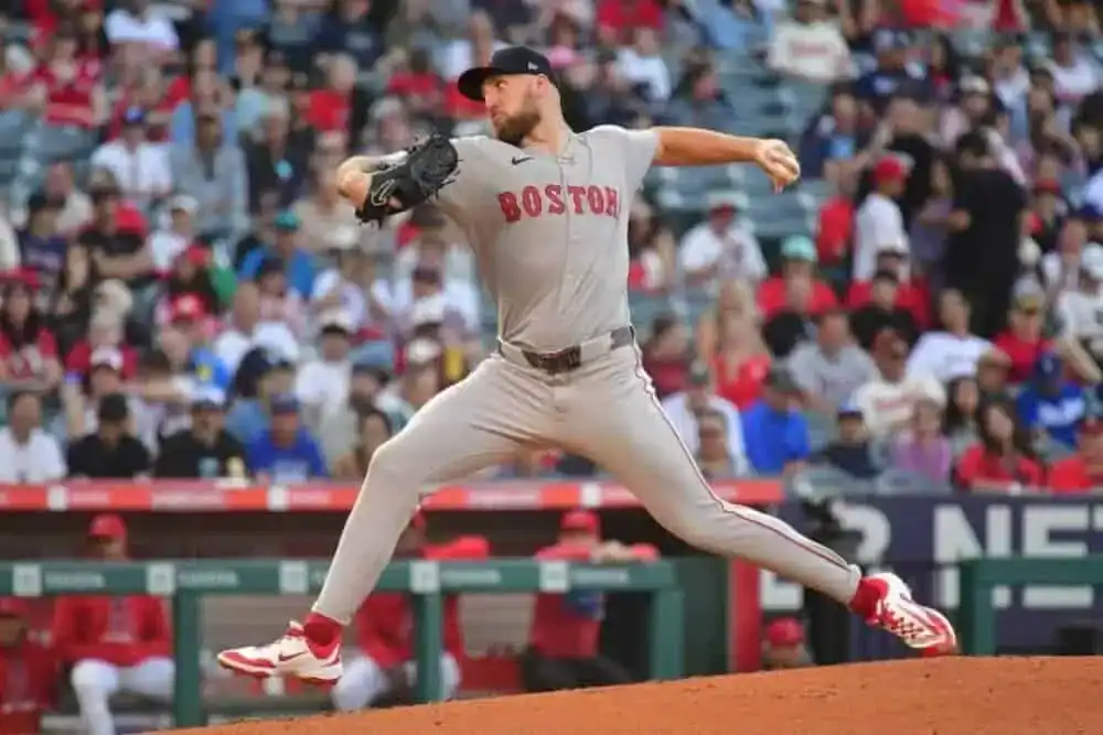 A baseball player is captured mid-action while throwing a ball. The scene takes place in an outdoor stadium, likely during a college baseball game in Boston.