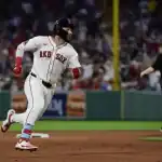 A Boston Red Sox player sprints towards base as the crowd cheers in the background, with an umpire observing the play.