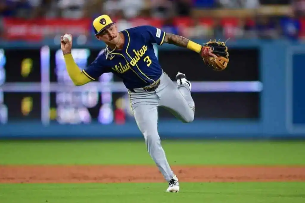 A Milwaukee Brewers player in a blue and yellow City Connect jersey throws a baseball across the infield.