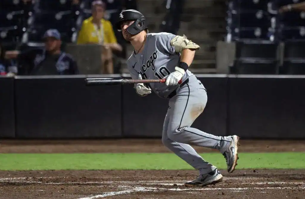 A baseball player in a gray uniform with "Chicago" on it runs towards first base, holding a bat, during a night game.