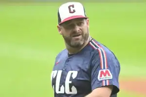 A baseball player in a blue jersey with "CLE" printed on it, wearing a cap with a 'C', stands on the field ready for action.