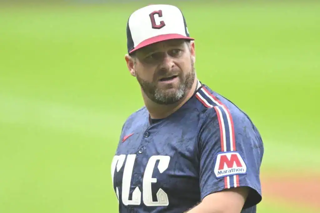 A baseball player in a blue jersey with "CLE" printed on it, wearing a cap with a 'C', stands on the field ready for action.