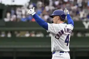 A baseball player wearing a blue and white striped jersey raises both arms in celebration on the field, with fans visible in the background.