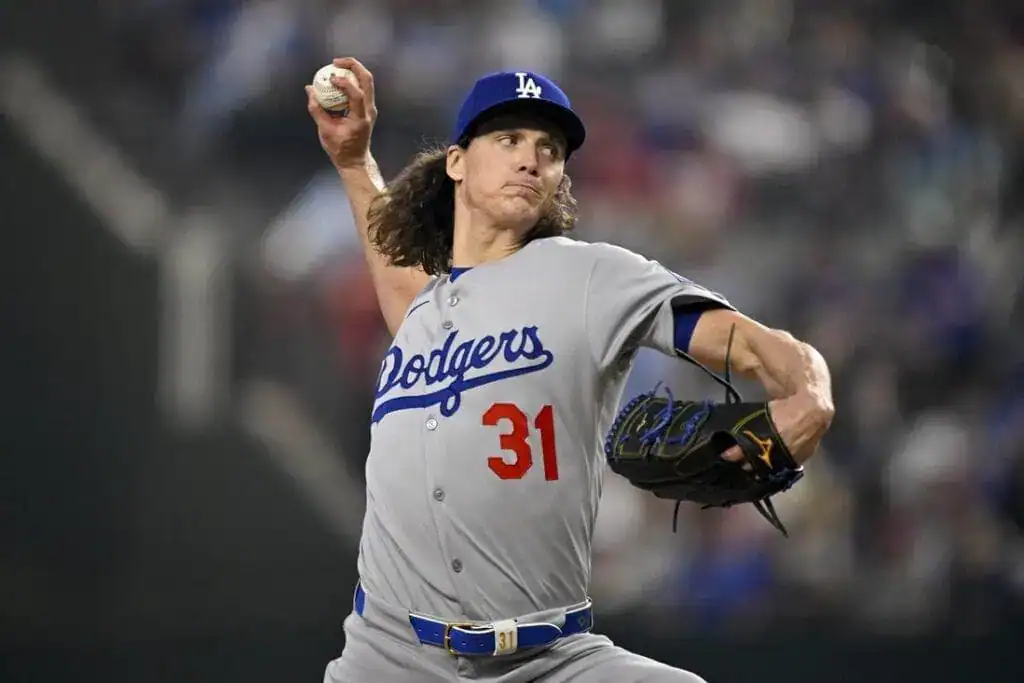A Los Angeles Dodgers pitcher in a gray uniform winds up to throw a baseball at a night game, showcasing intense focus and athleticism.