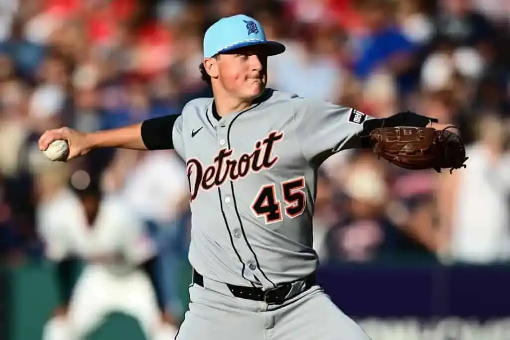 A pitcher in a grey Detroit Tigers uniform throws a baseball against a blurred lively crowd backdrop.