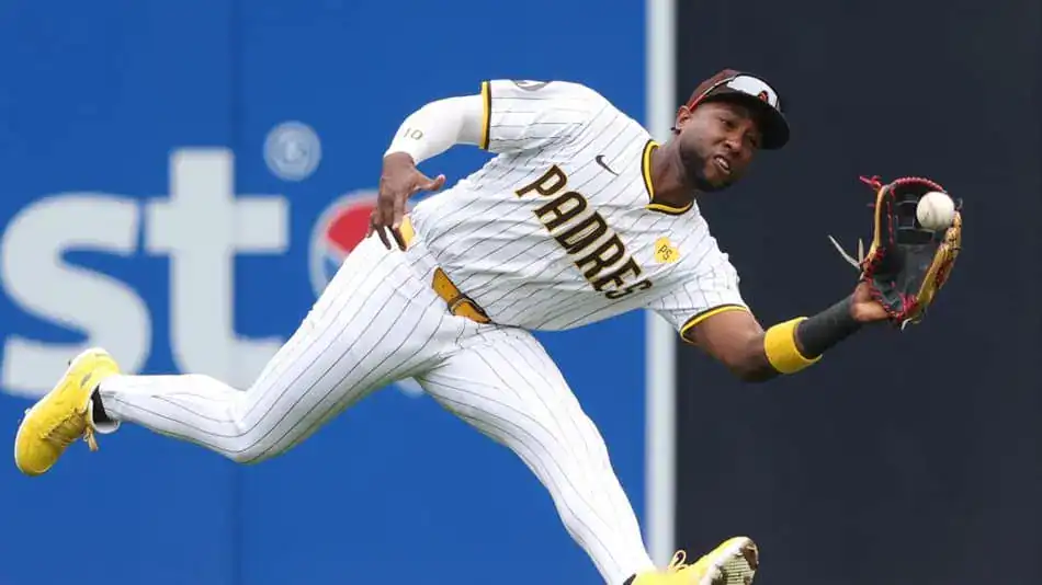 A baseball player in a white and brown striped uniform dives to catch a ball, showcasing athleticism and focus on the field.