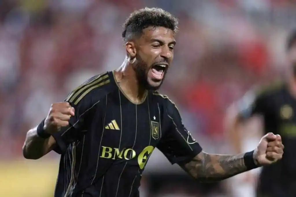 A man is wearing a black shirt and is likely engaged in a soccer game or activity. The setting appears to be an outdoor stadium, indicating an athletic environment.
