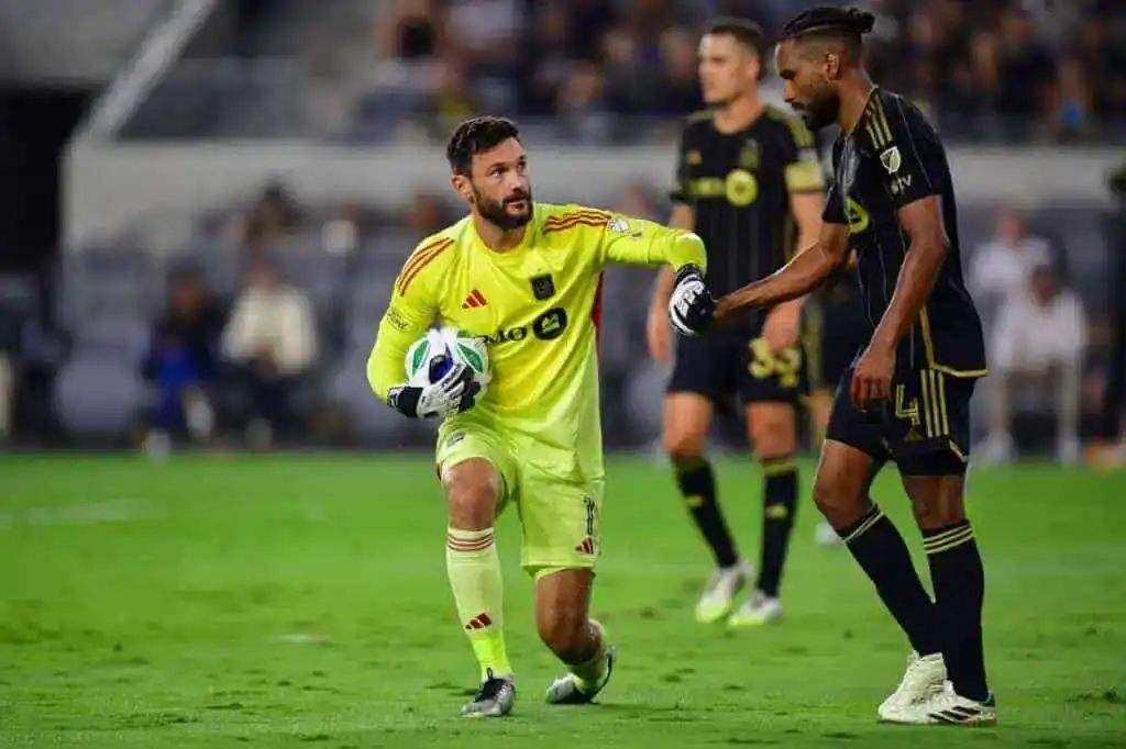 The image shows a soccer goalkeeper, wearing a yellow and green uniform, holding the ball.