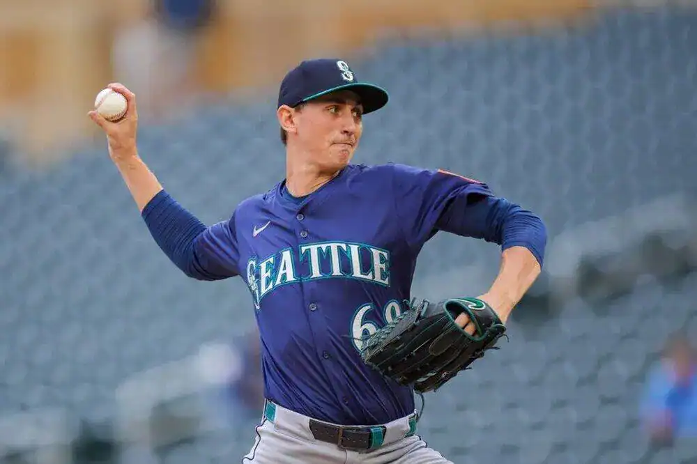 A man is throwing a baseball in Seattle. He is dressed in a baseball uniform, ready to participate in an athletic game.