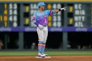 A baseball player stands confidently on the field, wearing a colorful jersey and pants, signaling to teammates with enthusiasm.