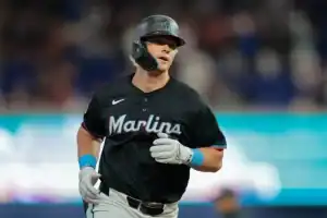 A Miami Marlins player runs towards the dugout, wearing a black jersey with bright accents, amidst a blurred crowd backdrop.
