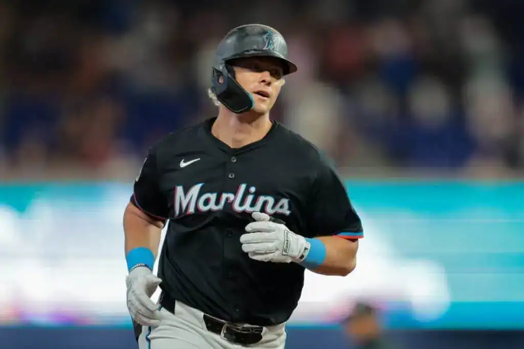 3 A Miami Marlins player runs towards the dugout, wearing a black jersey with bright accents, amidst a blurred crowd backdrop.
