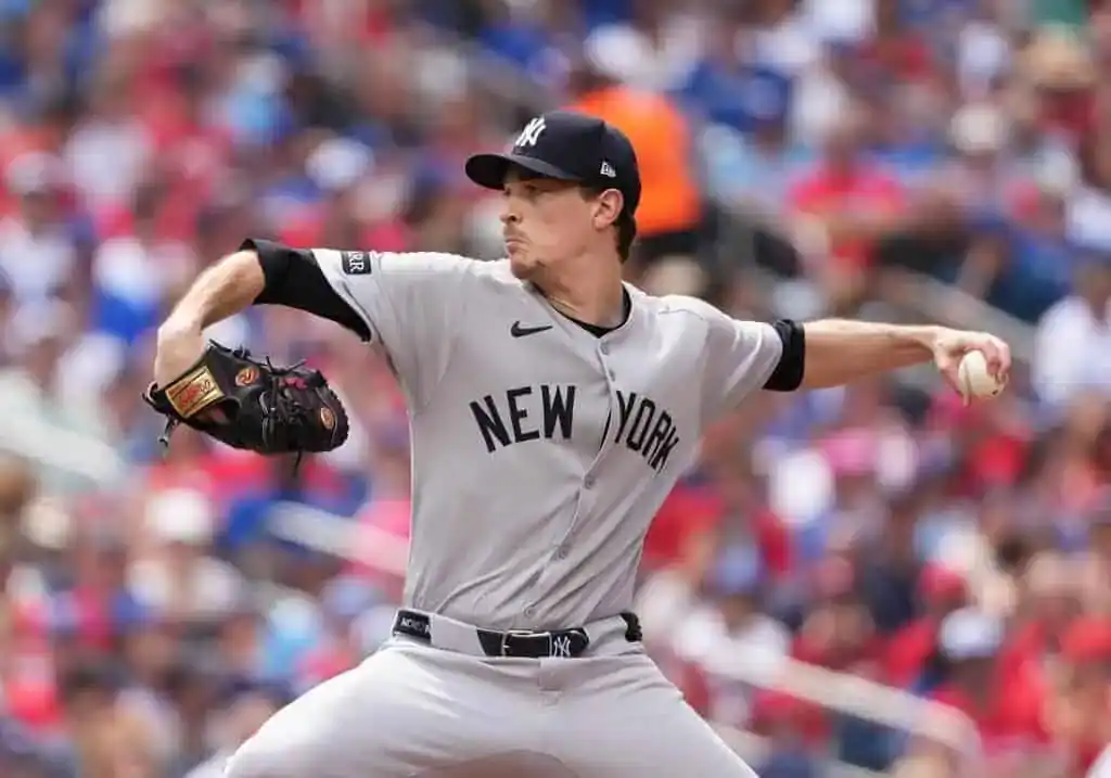 A baseball player is captured in action as he throws a ball. He is wearing a baseball uniform and protective gear
