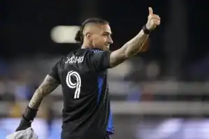 A soccer player in a black jersey with "Nacho" and the number 9 raises his thumb, celebrating a moment on the field.