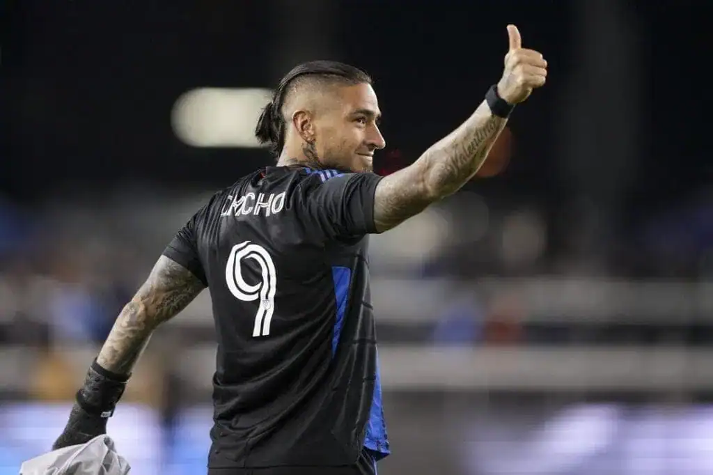 A soccer player in a black jersey with "Nacho" and the number 9 raises his thumb, celebrating a moment on the field.