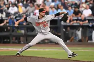 A pitcher in a gray Baltimore jersey winds up to throw, showcasing athleticism on a baseball field filled with spectators.