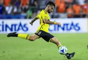 A soccer player in a bright yellow uniform strikes a ball across the grassy field during an intense match.