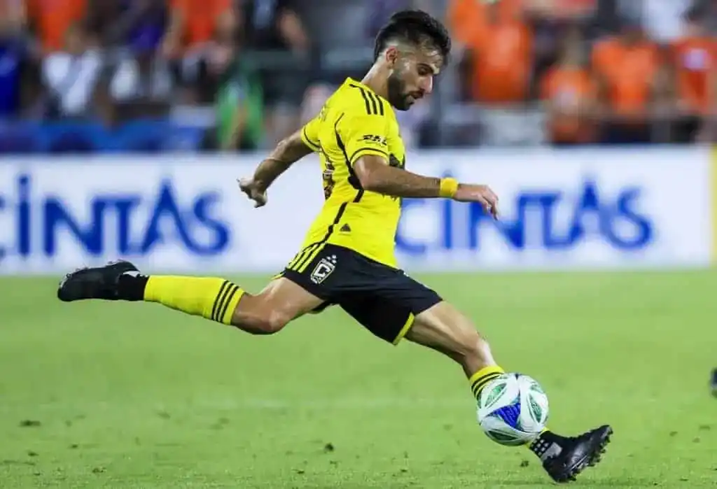 A soccer player in a bright yellow uniform strikes a ball across the grassy field during an intense match.
