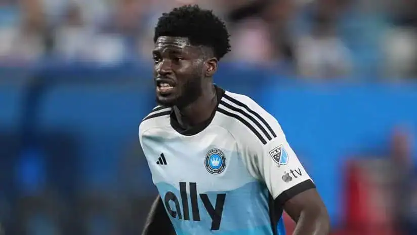 A soccer player in a light blue and white jersey with "ally" printed on it, sprinting on the field during a match.