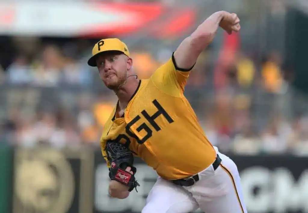 A baseball player in a yellow jersey, mid-pitch with intense focus, surrounded by a blurred stadium crowd during a game.