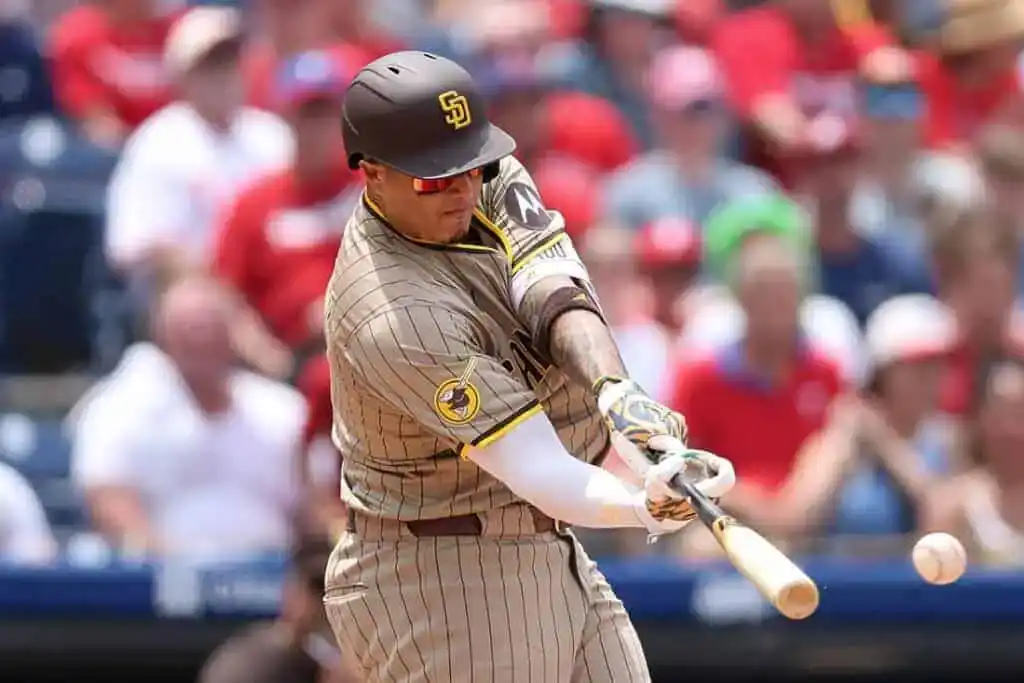 A baseball player in a striped brown and yellow uniform swings a bat at a pitch during a game, with a cheering crowd in the background.