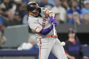 A San Francisco Giants player swings a bat during a baseball game, surrounded by fans in the stadium.