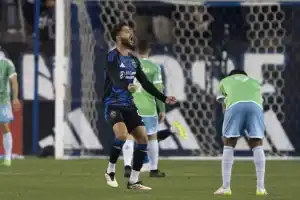 A soccer match in progress, featuring players in blue and green uniforms, with a goal net in the background. Celebratory and focused actions are captured.
