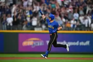 A Seattle Mariners player in a royal blue and yellow City Connect jersey celebrates as he runs the bases.