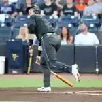 A baseball player swings a bat, preparing to hit the ball, with a stadium filled with cheering fans in the background.