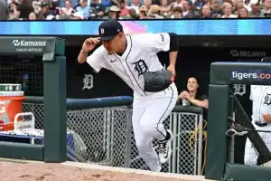 A baseball player wearing a white uniform with a "D" logo runs out of the dugout toward the field, with fans watching in the background.