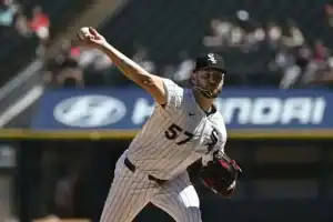 A baseball pitcher in a white and black striped uniform throws a ball from the mound, with an empty stadium backdrop.