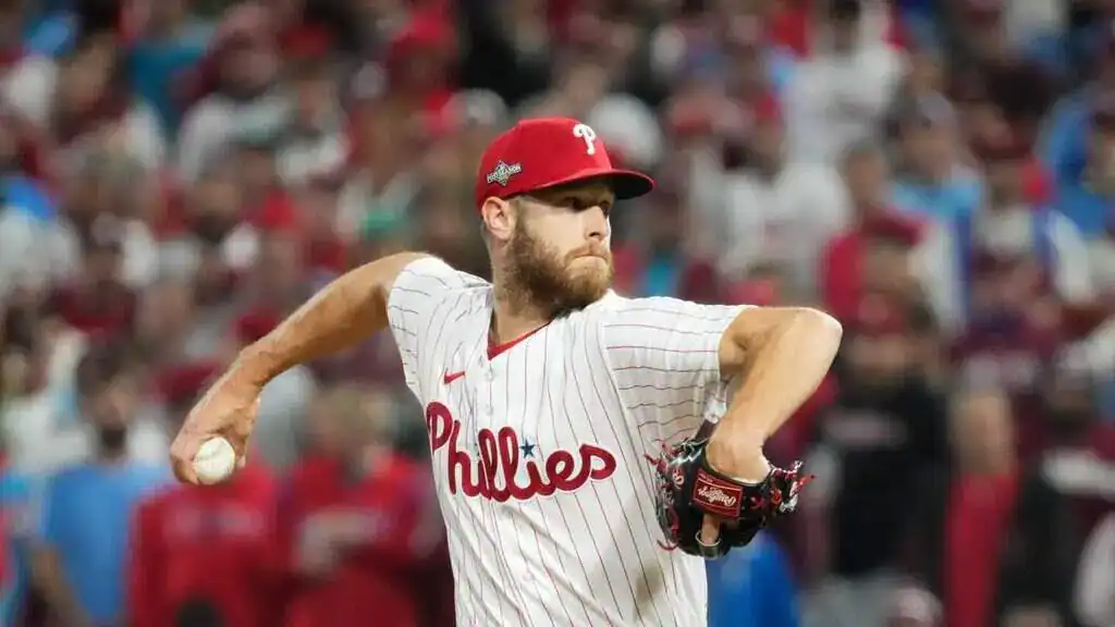 A Philadelphia Phillies pitcher winds up to throw during a game, surrounded by a cheering crowd in the stands.