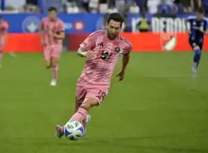 A man is wearing a pink football uniform and is in the act of kicking a soccer ball. The setting appears to be an outdoor field with grass, indicative of a sport-related environment.