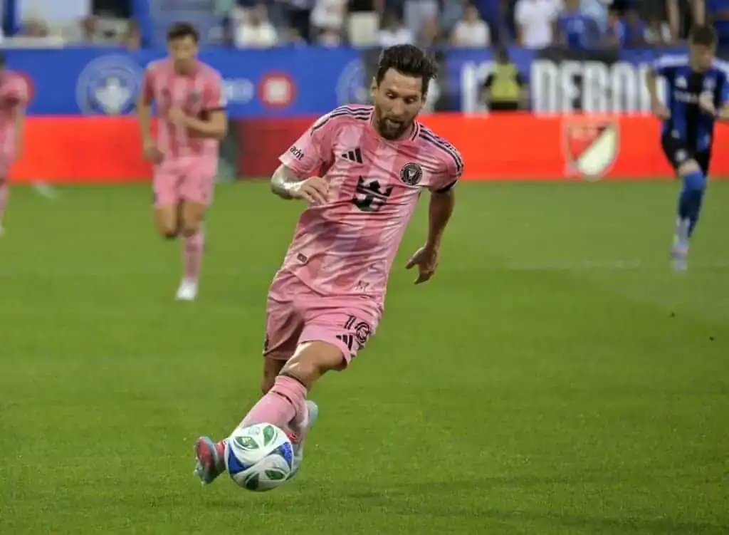 A man is wearing a pink football uniform and is in the act of kicking a soccer ball. The setting appears to be an outdoor field with grass, indicative of a sport-related environment.