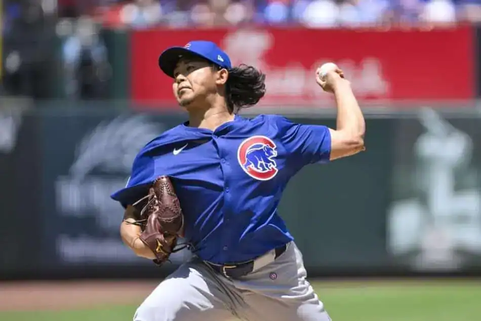 The image shows a Chicago Cubs baseball player throwing a ball. He's wearing a blue uniform with the Cubs logo and is in the middle of his throwing motion.