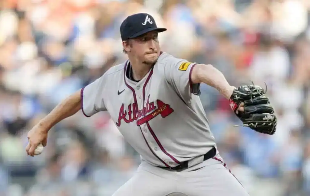 A baseball pitcher in an Atlanta Braves uniform winds up to throw, showcasing athletic form against a blurred crowd backdrop.