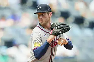A pitcher in a gray Atlanta Braves jersey prepares to throw a baseball during a game in a crowded stadium.