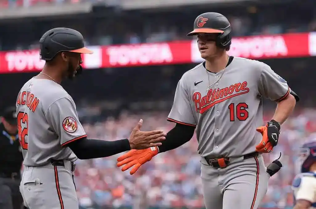 Two baseball players in gray Baltimore Orioles uniforms celebrate with a high-five on the field during a game.