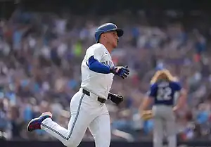 Toronto Blue Jays player runs the bases after making contact, with the crowd cheering in the background during an MLB game.